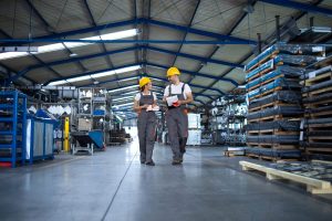 factory-workers-work-wear-yellow-helmets-walking-through-industrial-production-hall-discussing-about-delivery-deadline